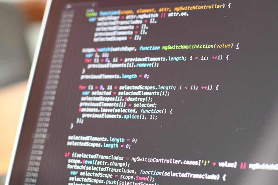 A close-up image of a computer screen displaying colorful lines of HTML and CSS code in a dark-themed editor, with various tags, selectors, and attributes visible. The screen shows a mixture of red, g